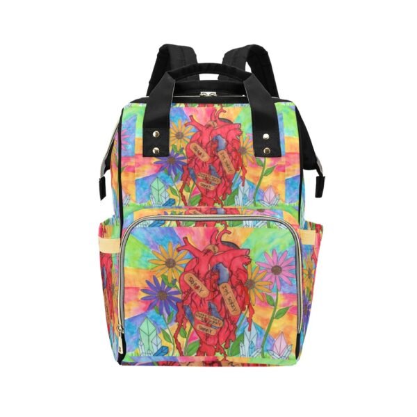 Multi-function backpack featuring a striking blooming heart art print. At the center, a large anatomical heart is adorned with bandages that read 'SORRY' and 'I'M SORRY,' surrounded by vibrant flowers and crystal-like shapes against a colorful rainbow backdrop. The backpack includes black straps and handles, a front zippered pocket, and side compartments, blending emotional symbolism with artistic expression. An original Imaginables creation combining wearable art with everyday practicality